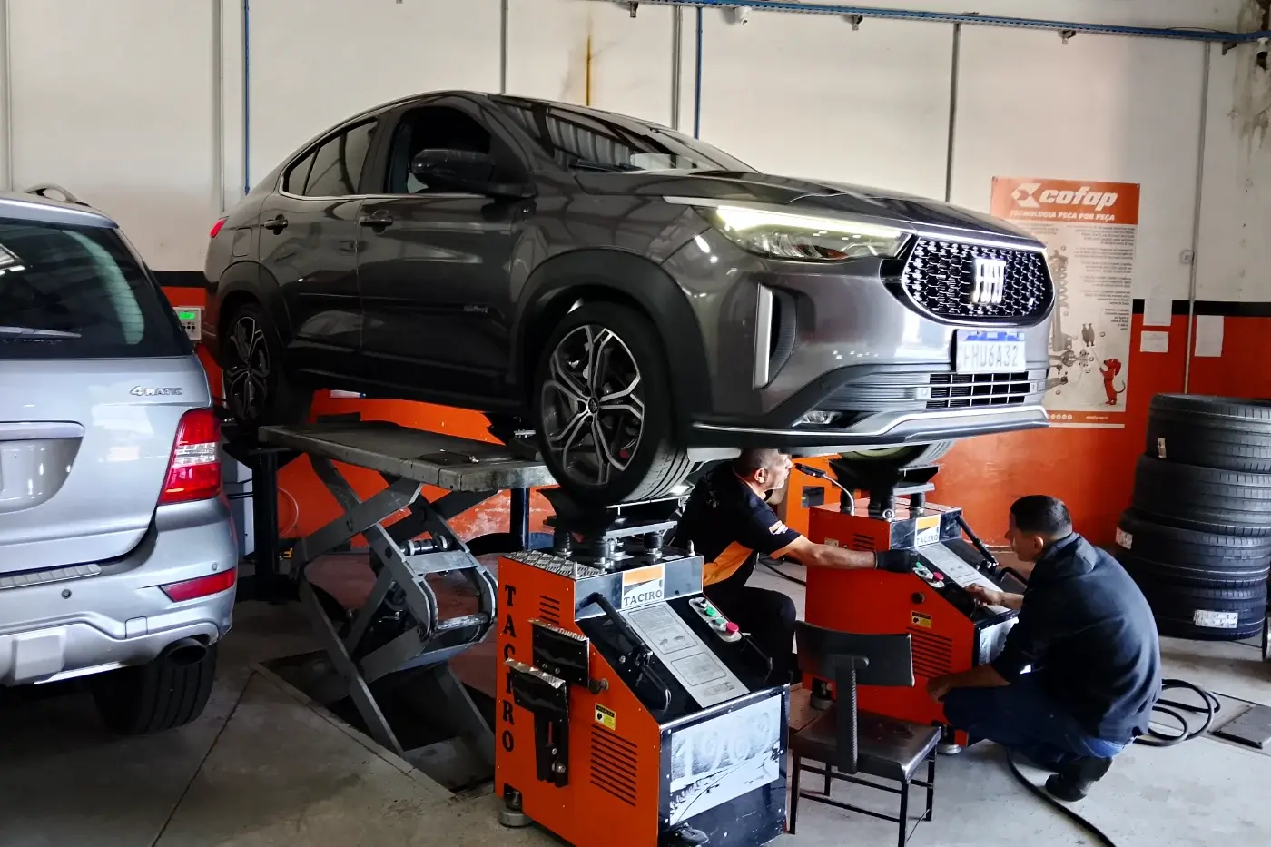 Fiat Fastback suspensa no elevador com duas máquinas de balanceamento laranja embaixo das rodas, que continuam montadas no carro