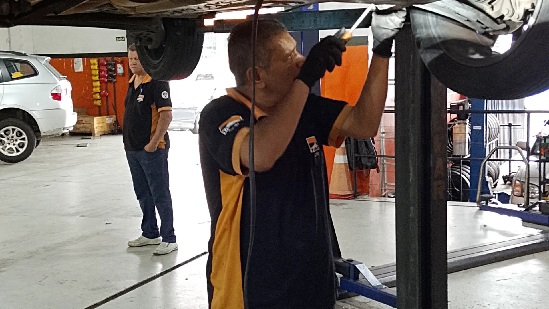 Mecânico da Taciro com uma sonda embaixo de um carro suspenso no elevador, procurando de onde vem o ruído
